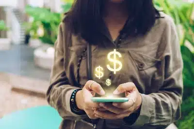 Una mujer usa un smartphone del que emergen hologramas brillantes con el símbolo de dólar ($).