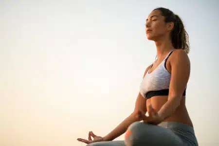 Una mujer practica meditación en una postura de yoga con los ojos cerrados y expresión serena.