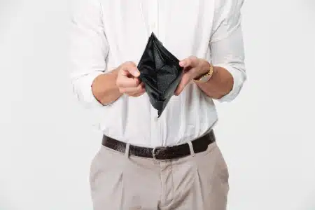 Un hombre sostiene una billetera negra abierta y completamente vacía frente a su torso.