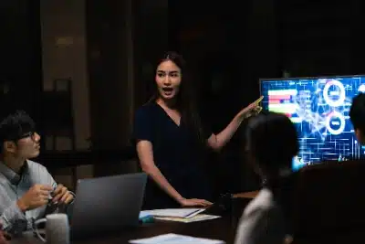 mujer joven realizando una presentación y señalando una pantalla que muestra gráficos de datos complejos