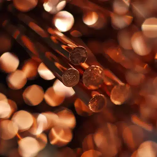 Un primer plano de varios cables de cobre redondos y brillantes cortados de frente, con un fondo difuminado lleno de luces doradas y cobrizas