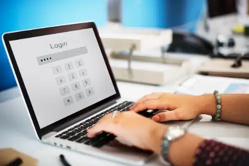 se observan las manos de una persona escribiendo en el teclado de una laptop, cuya pantalla muestra una interfaz de inicio de sesión con un teclado numérico digital para ingresar un PIN o contraseña