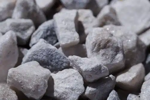 se muestra un primer plano detallado de pequeñas piedras o grava de color blanco y gris con texturas rugosas bajo la luz del sol.