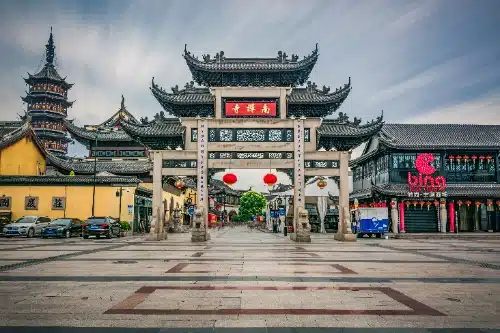 Un paifang tradicional chino da entrada a una plaza rodeada de edificaciones de arquitectura clásica, con una pagoda octogonal a la izquierda.