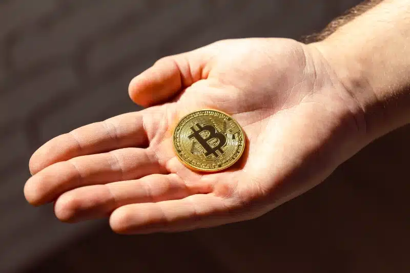 Mano abierta sosteniendo una moneda dorada de bitcoin en la palma.